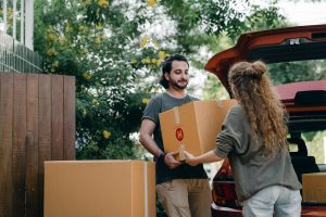 a man and a woman carrying boxes to move during the summer.