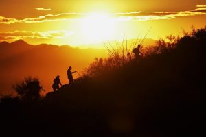 People are hiking up a crest, and there is a sunset over mountains in Tucson National Park.