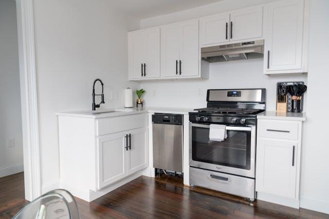 Compact white kitchen with stainless steel appliances and dark wood flooring in a modern guest house